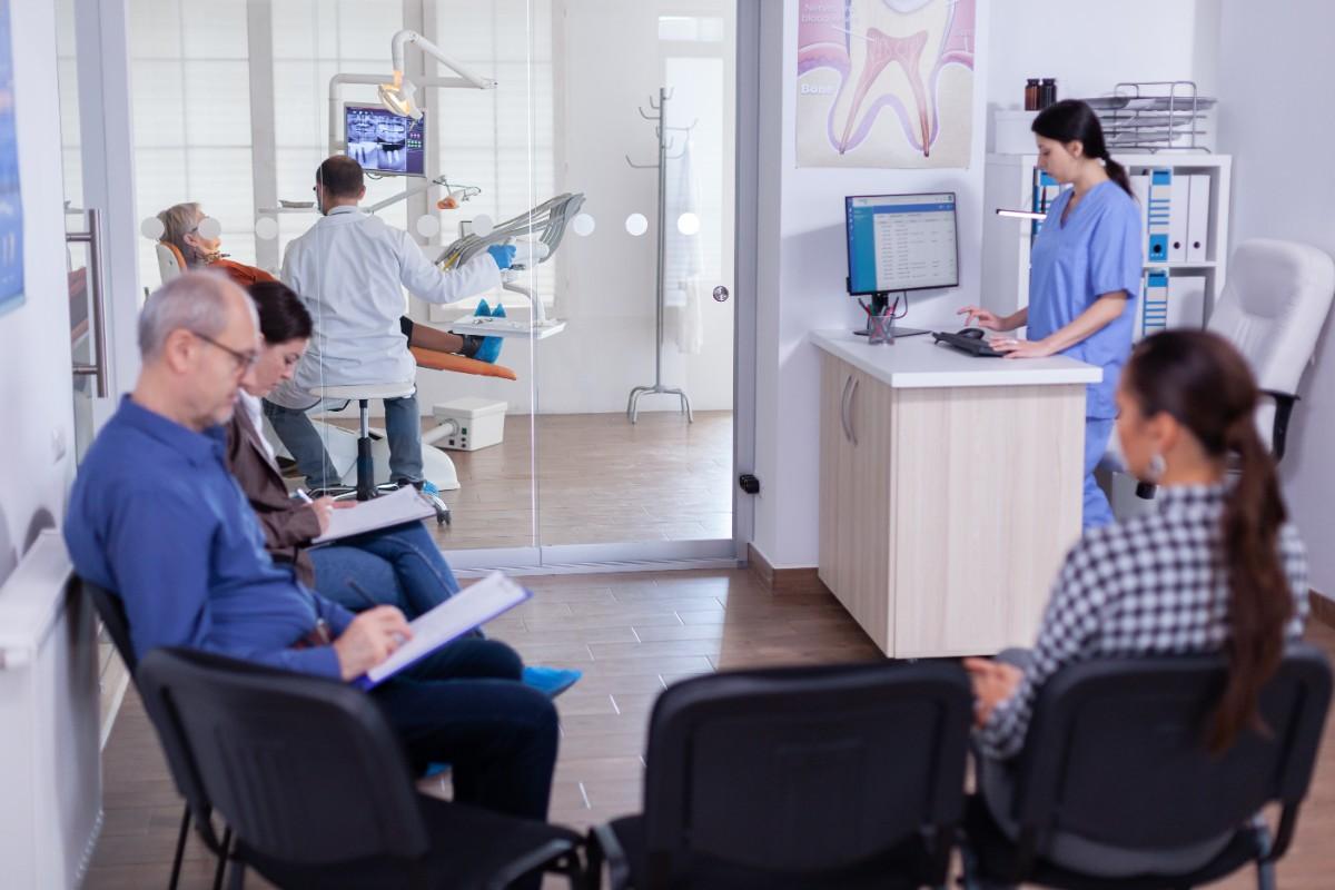 Dental clinic waiting area with patients seated and staff assisting patients during appointments.