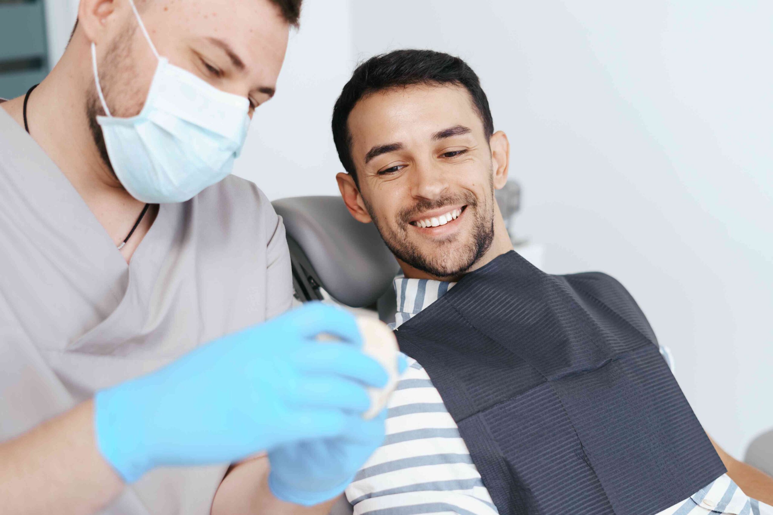 Dentist examining a smiling male patient during a dental appointment.